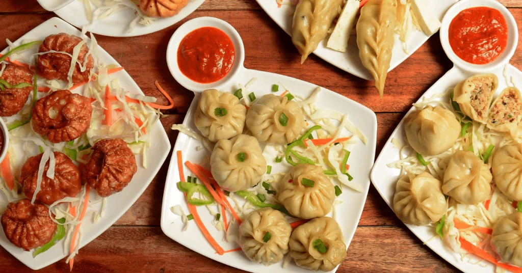 A variety of steamed and fried momos garnished with fresh vegetables, served with red chili sauce, a potential diabetic-friendly meal option